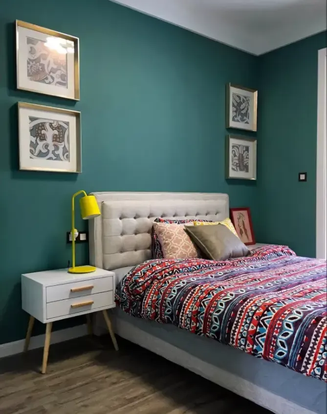 孔雀绿的墙面对称点缀金框装饰画,卡其色软靠床搭配线条简约的床头柜